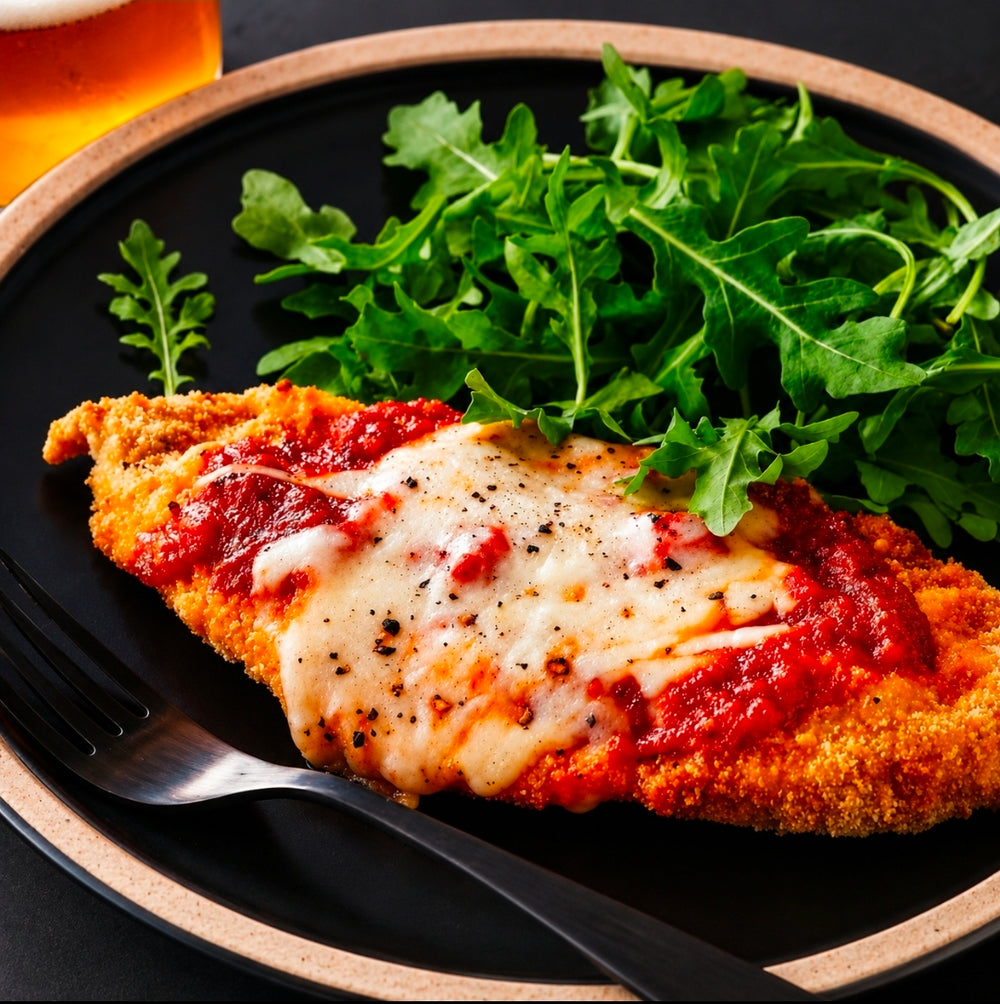 Poulet parmigiana pané avec sauce tomate et fromage gratiné servi sur assiette noire par Aliments DKL