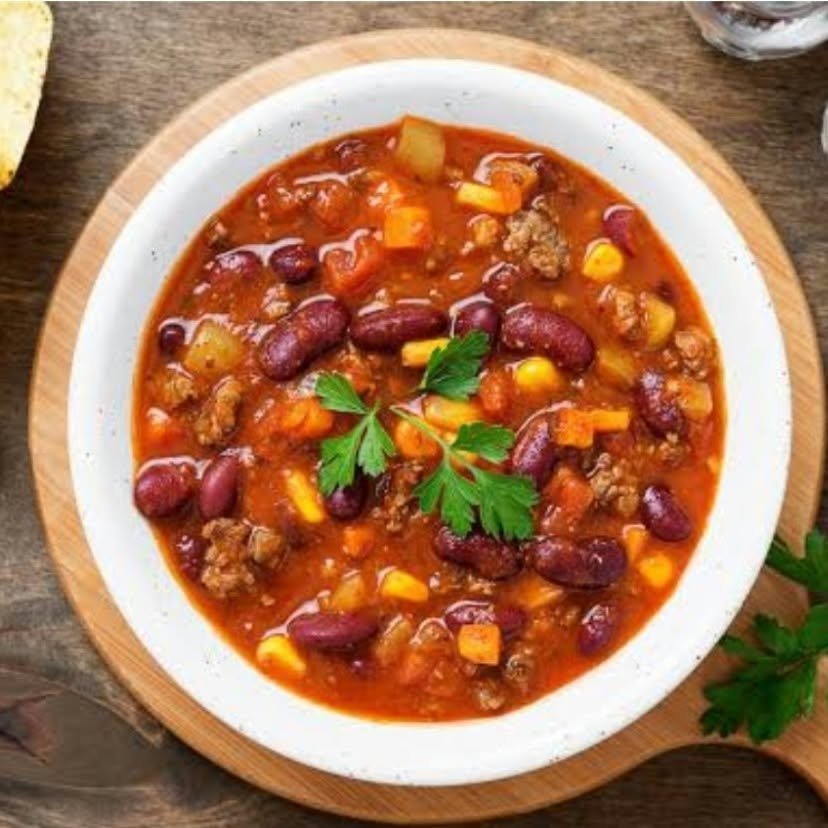 Bol de chili texan au bœuf haché, haricots rouges, maïs et légumes, garni de persil et accompagné de croustilles de maïs. Une spécialité Aliments DKL.